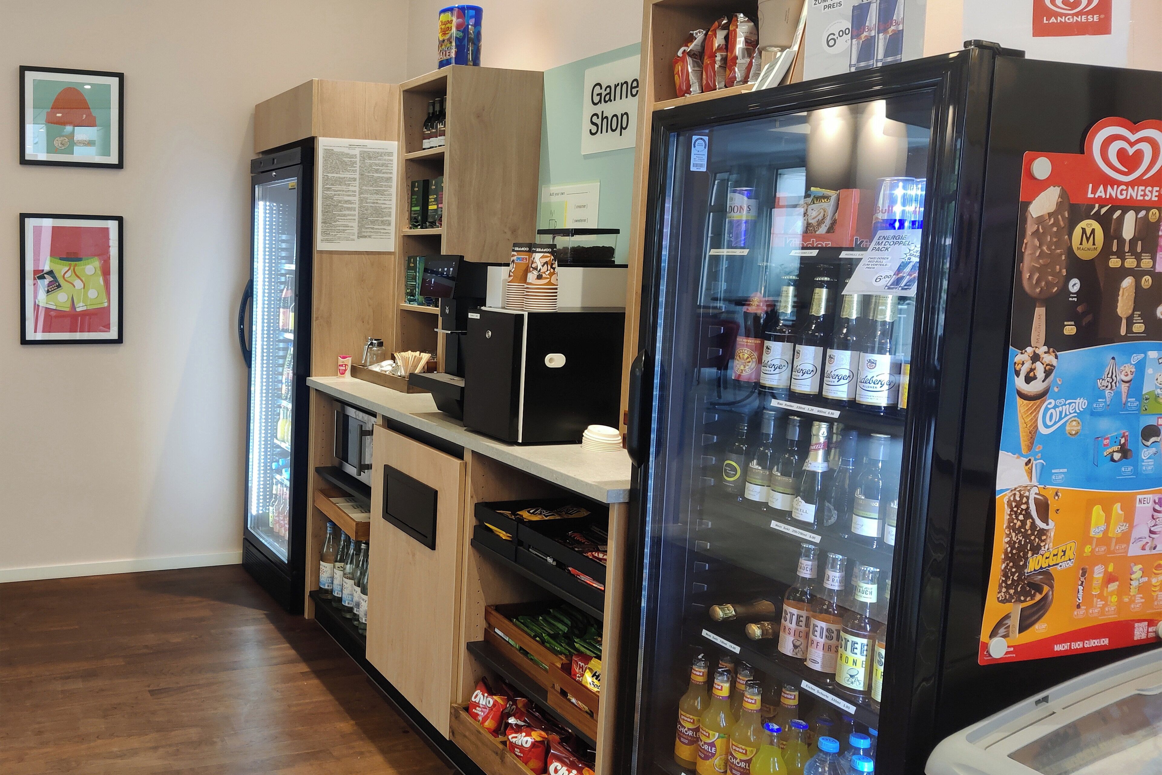 A refrigerated display with various beverages and snacks, a coffee machine, and a sign for a 'Garn Shop'.