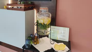 Un dispensador de jugo con un letrero, vasos y una cesta de pan sobre una mesa.