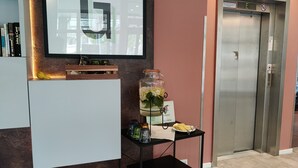 A reception area with a large 'G' sign, a glass jar with flowers and lemons, a small table with a plate and napkin, and an elevator. - Garner Hotel Wiesbaden City by IHG (Wiesbaden)