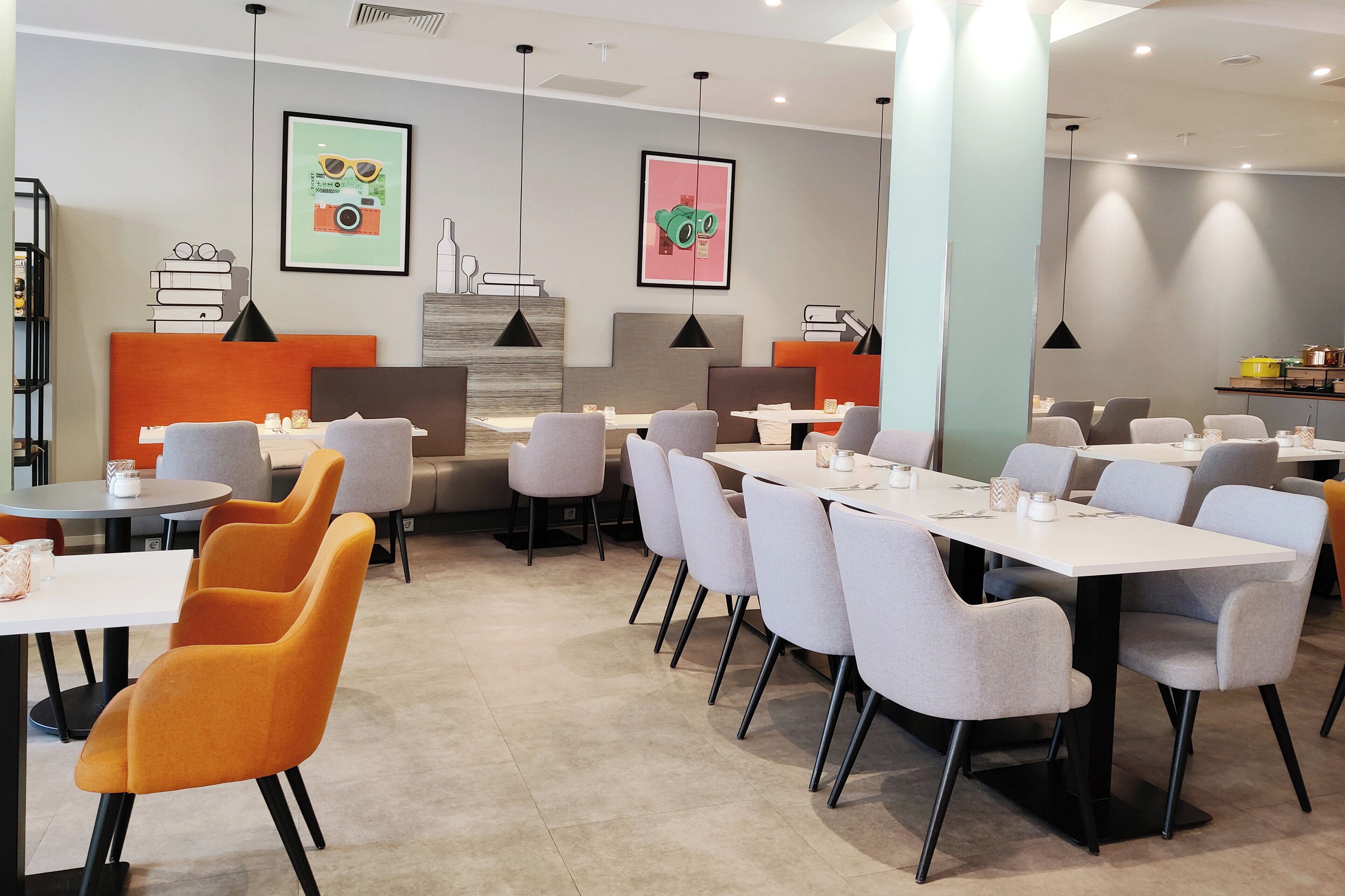 A modern dining area with multiple tables and chairs, framed artwork on the walls, and a bookshelf.