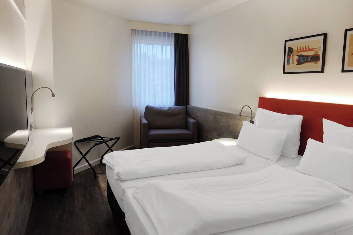 Habitación de hotel con dos camas, un escritorio, una silla y un televisor.