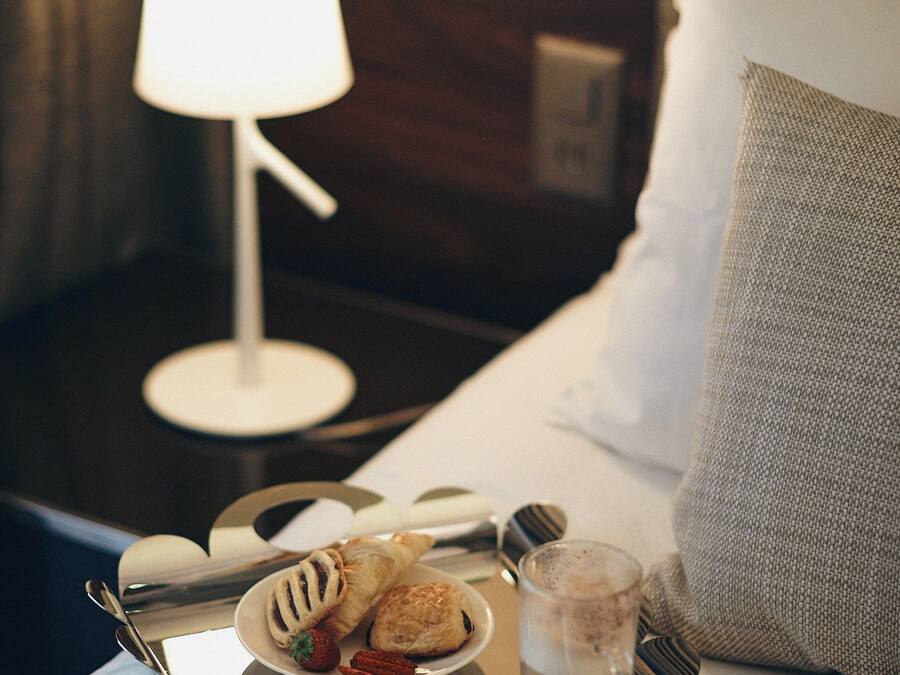 A neatly made breakfast tray with pastries, a glass of beverage, and cutlery on a hotel bed.