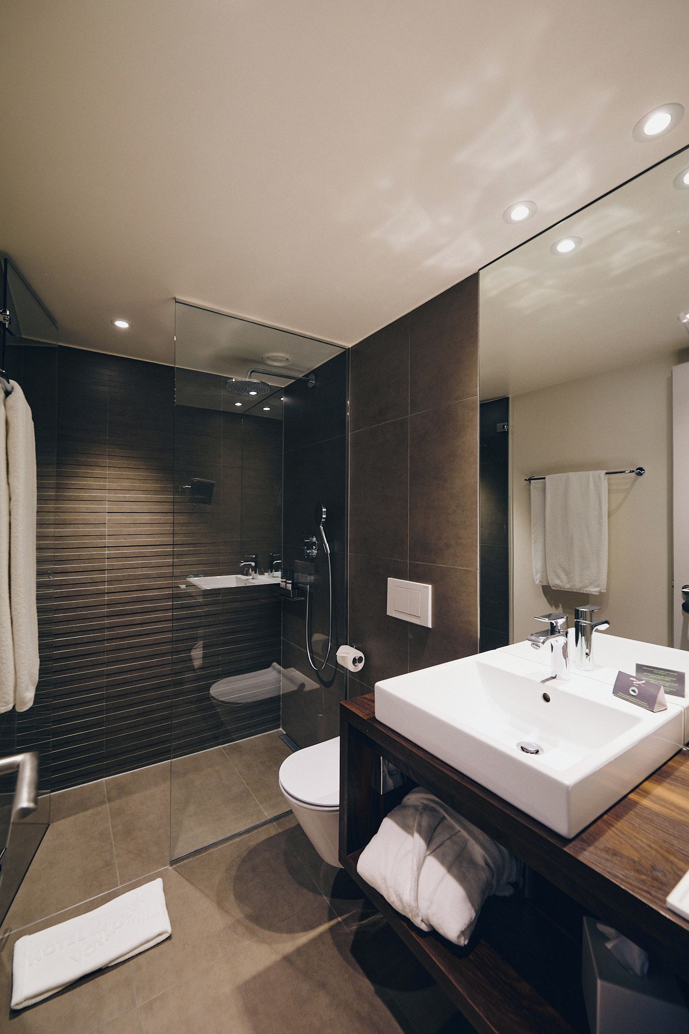 A modern bathroom with a large mirror, a white sink, a glass-enclosed shower, and a toilet.