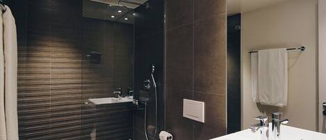 A modern bathroom with a large mirror, a white sink, a glass-enclosed shower, and a toilet.