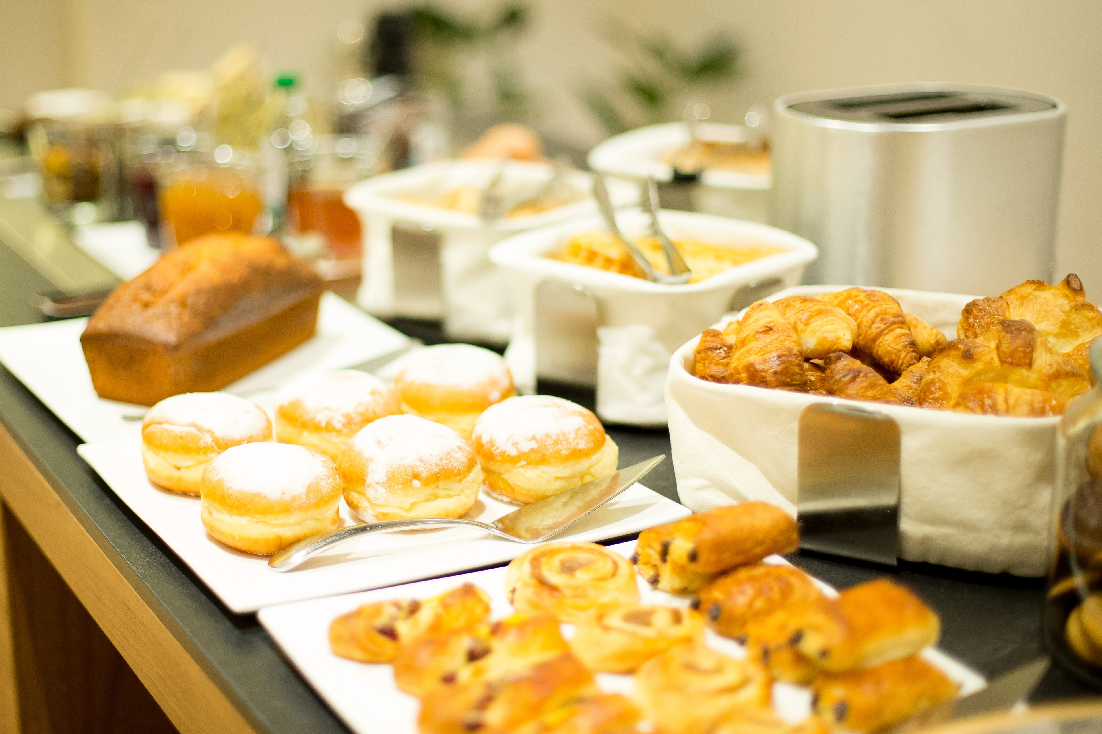Ein Buffet mit verschiedenen Backwaren und Gebäck, darunter Croissants und Muffins, präsentiert auf Serviertabletts.