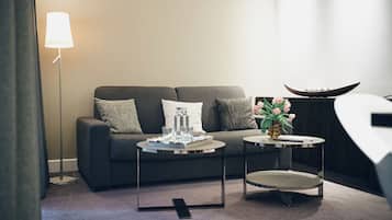 Ein modernes Wohnzimmer mit einem grauen Sofa, zwei Beistelltischen, einer Stehlampe und einer Vase mit Blumen.