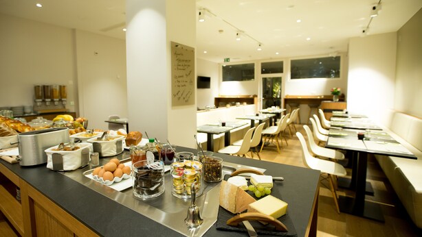 Un buffet per la colazione con diversi cibi e una zona salotto con tavoli e sedie.