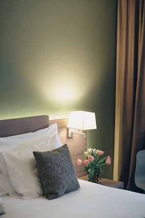 A hotel room with a bed, pillows, a nightstand with a lamp, and a vase with flowers. - Hôtel des Voyageurs (Lausanne)