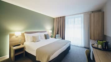 Ein Hotelzimmer mit einem Bett, Nachttischen, einem Schreibtisch und einem fensterbepflanzten Fenster.