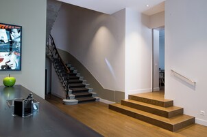 Una escalera moderna con escalones de madera y barandilla de metal, que conduce a un rellano en el segundo piso.