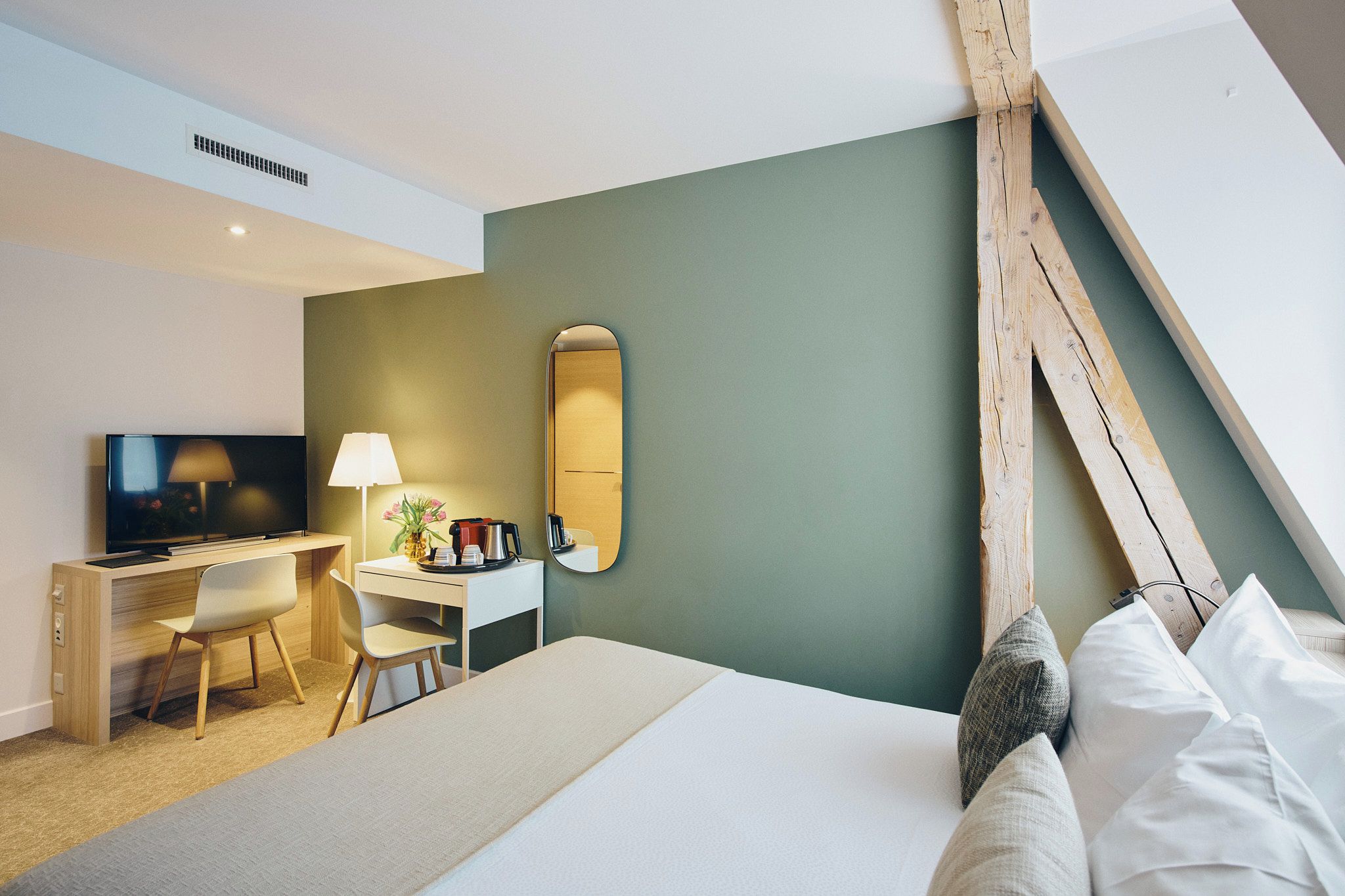 A hotel room with a bed, a desk, a chair, a television, a lamp, and a mirror.