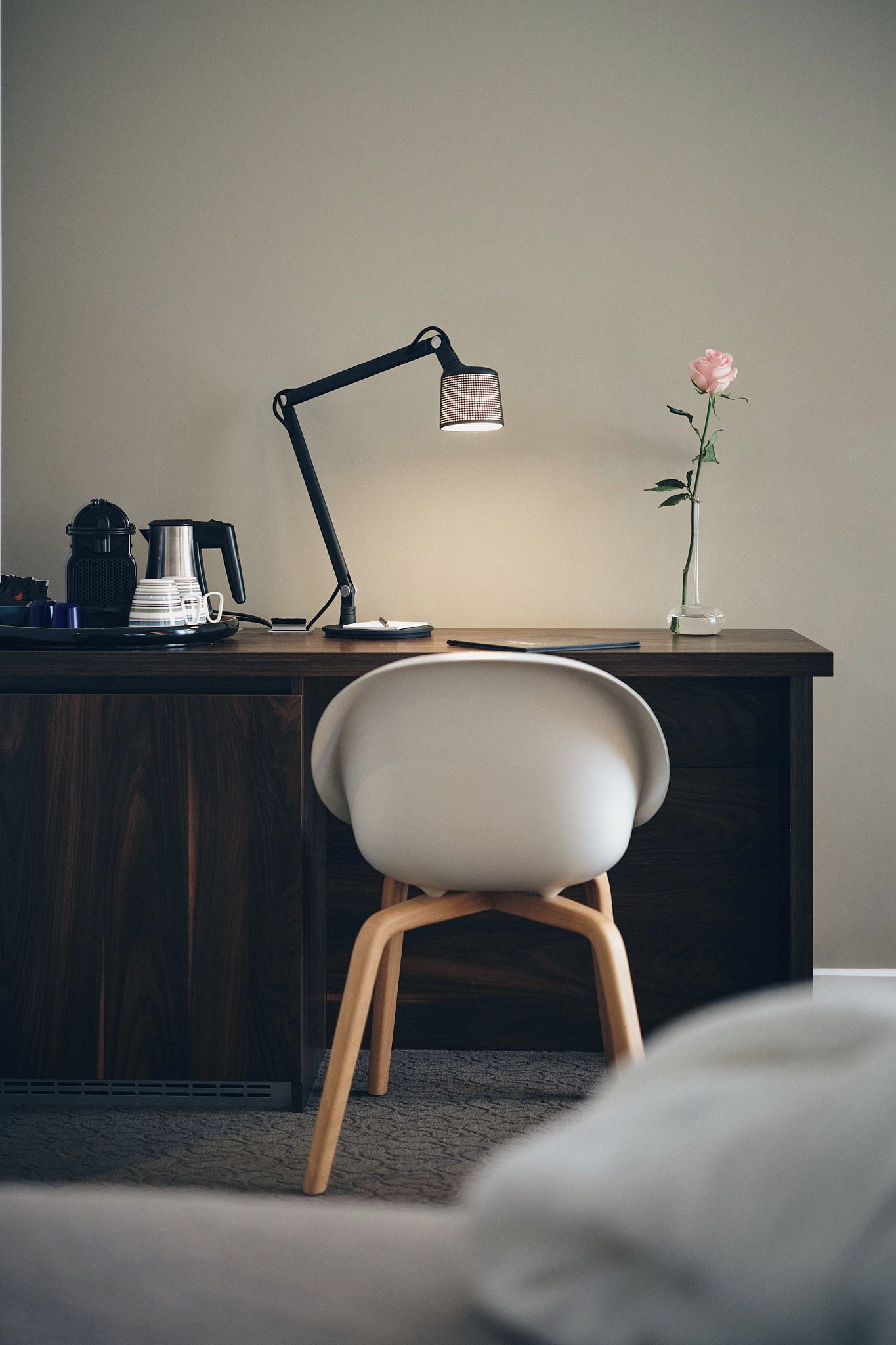 Een bureau met een lamp, een koffiezetapparaat en een vaas met een bloem.