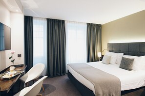 A hotel room with a bed, bedside table, lamp, chair, and a desk with a rose and a cup. - Hôtel des Voyageurs (Lausanne)