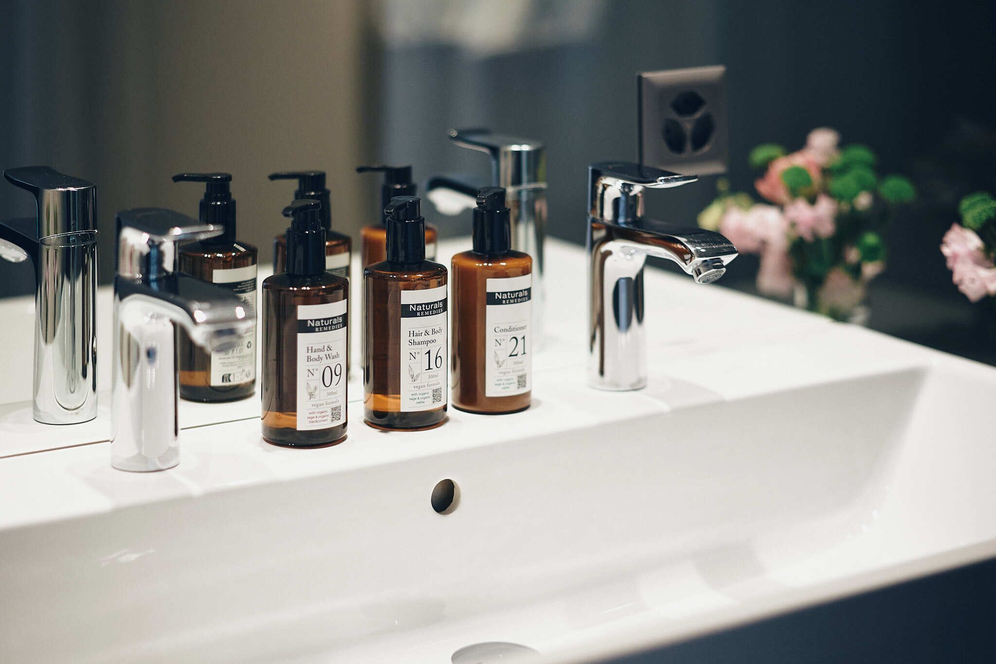 A bathroom sink with various toiletries including hand and body wash, shampoo, and conditioner.
