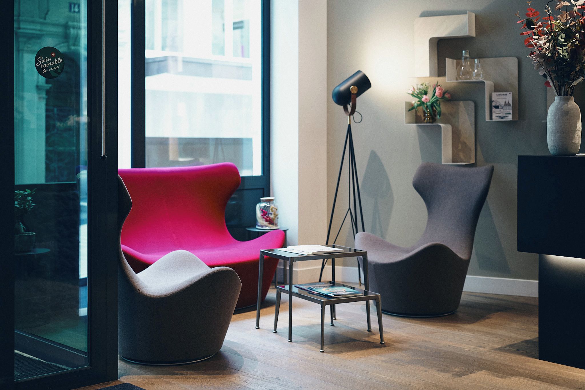 A modern interior with a red chair, a grey chair, a small table, and a floor lamp.