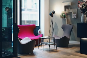 Un interior moderno con una silla roja, una silla gris, una mesita y una lámpara de pie.