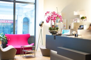 Una zona de recepción moderna con un interior luminoso, un amplio ventanal y un sofá rojo.