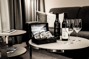 Habitación de hotel con una mesa redonda que presenta una botella de vino, dos copas de vino y una caja de bombones.