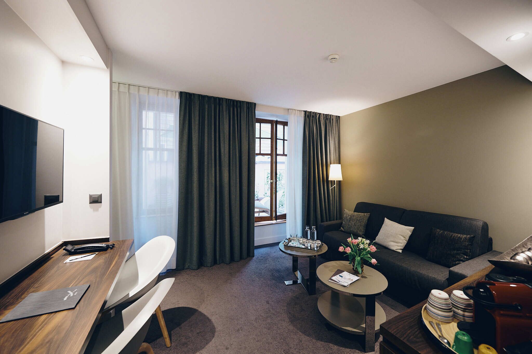 Une chambre d’hôtel équipée d’un téléviseur à écran plat, d’un bureau en bois, d’un canapé, d’une table basse et d’une table à manger avec des chaises.