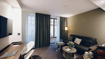 Une chambre d’hôtel équipée d’un téléviseur à écran plat, d’un bureau en bois, d’un canapé, d’une table basse et d’une table à manger avec des chaises.