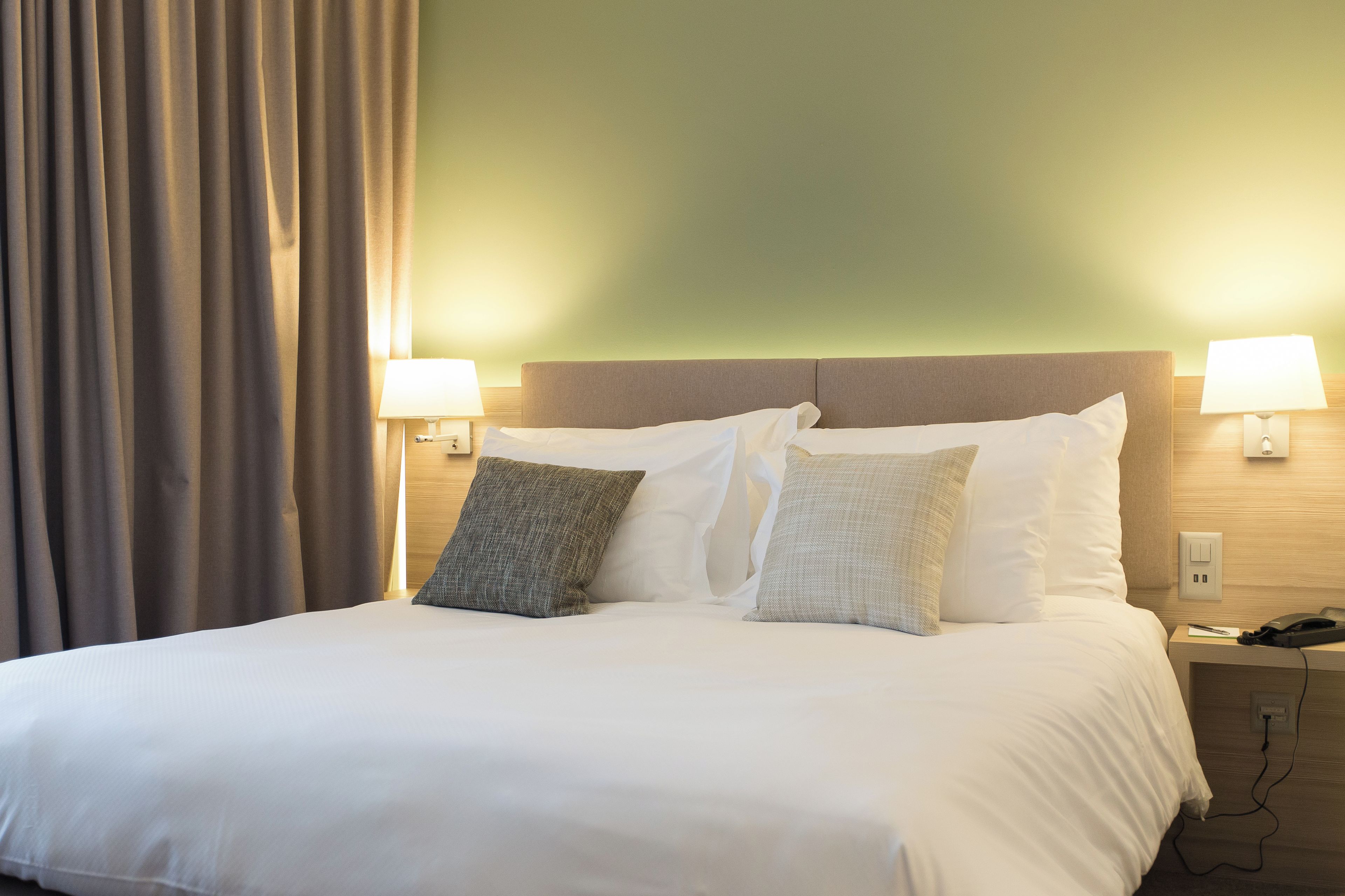 Ein Hotelzimmer mit einem Bett, zwei Nachttischlampen, einem Nachttisch und einem Vorhang.