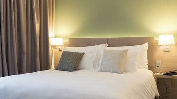 A hotel room with a bed, two bedside lamps, a nightstand, and a curtain.
