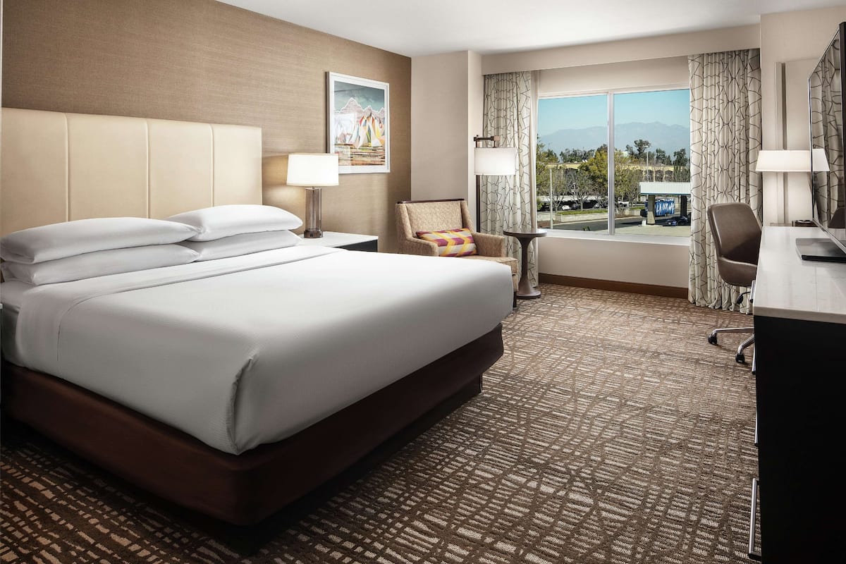 Ein Hotelzimmer mit einem großen Bett, einem Schreibtisch, einem Stuhl und Blick ins Freie.