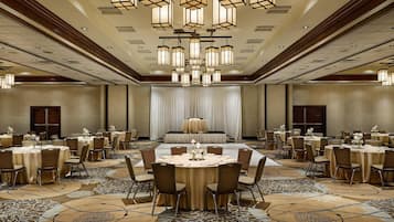 Un amplio salón de banquetes con mesas redondas, sillas y un escenario para presentaciones.
