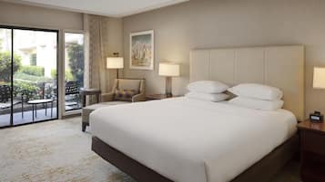 A hotel room with a large bed, a chair, a small table, a nightstand, a lamp, and a painting on the wall.