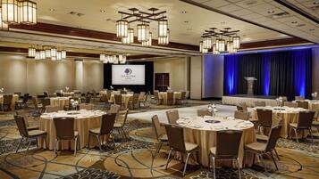 A conference room with round tables, chairs, and a stage with a podium.