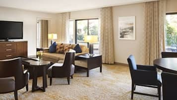 A hotel room with a sofa, two armchairs, a coffee table, a TV, and a dining table.