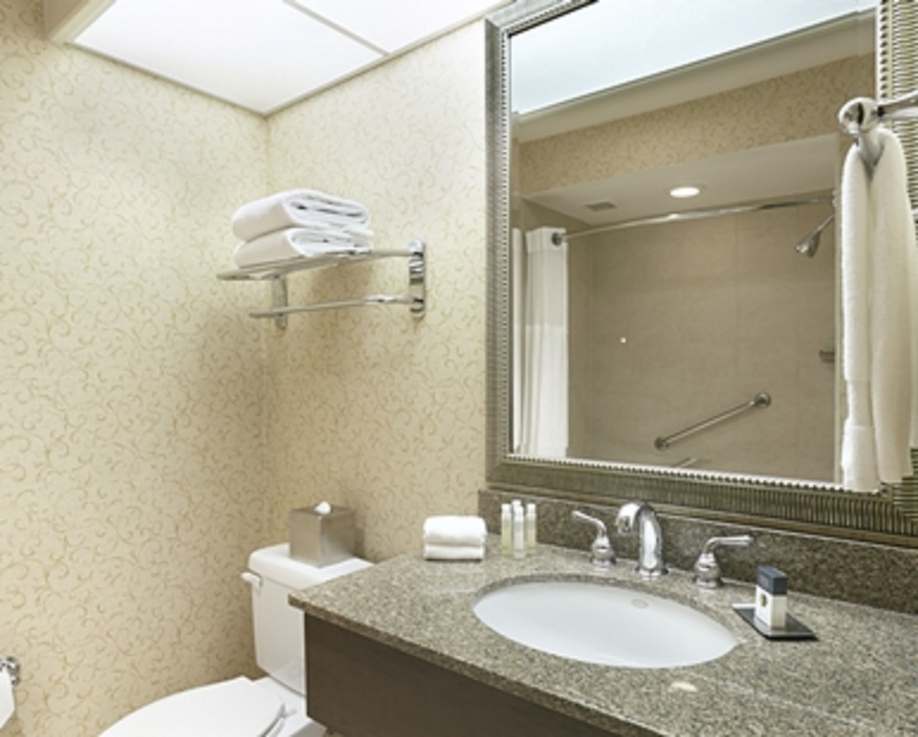 A bathroom with a sink, toilet, and shower. There are towels on a rack and a mirror above the sink.