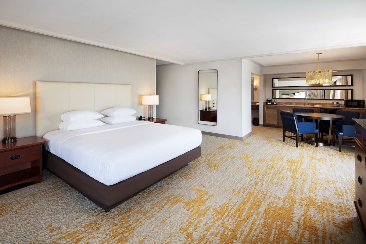 Ein Hotelzimmer mit einem großen Bett, Nachttischen, einem Schreibtisch mit Stühlen, einem Spiegel und einer Kristallleuchtre.