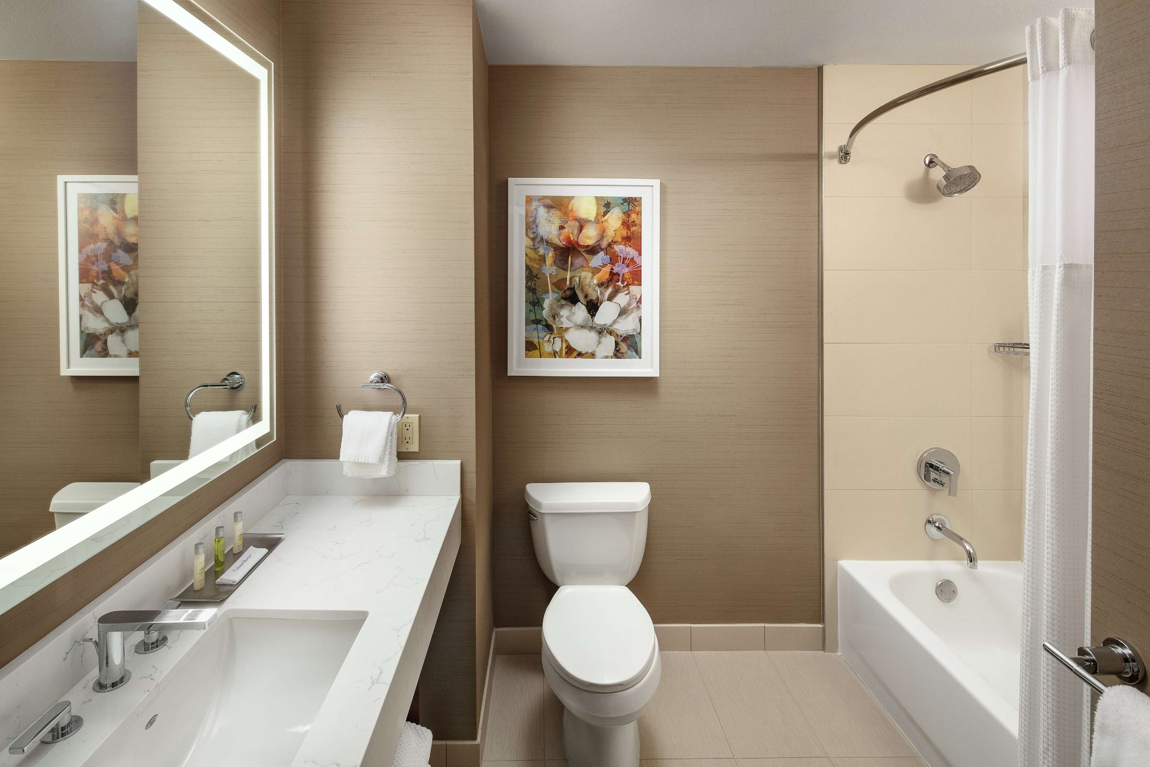 A modern bathroom with a large mirror, a white sink, a toilet, and a bathtub.