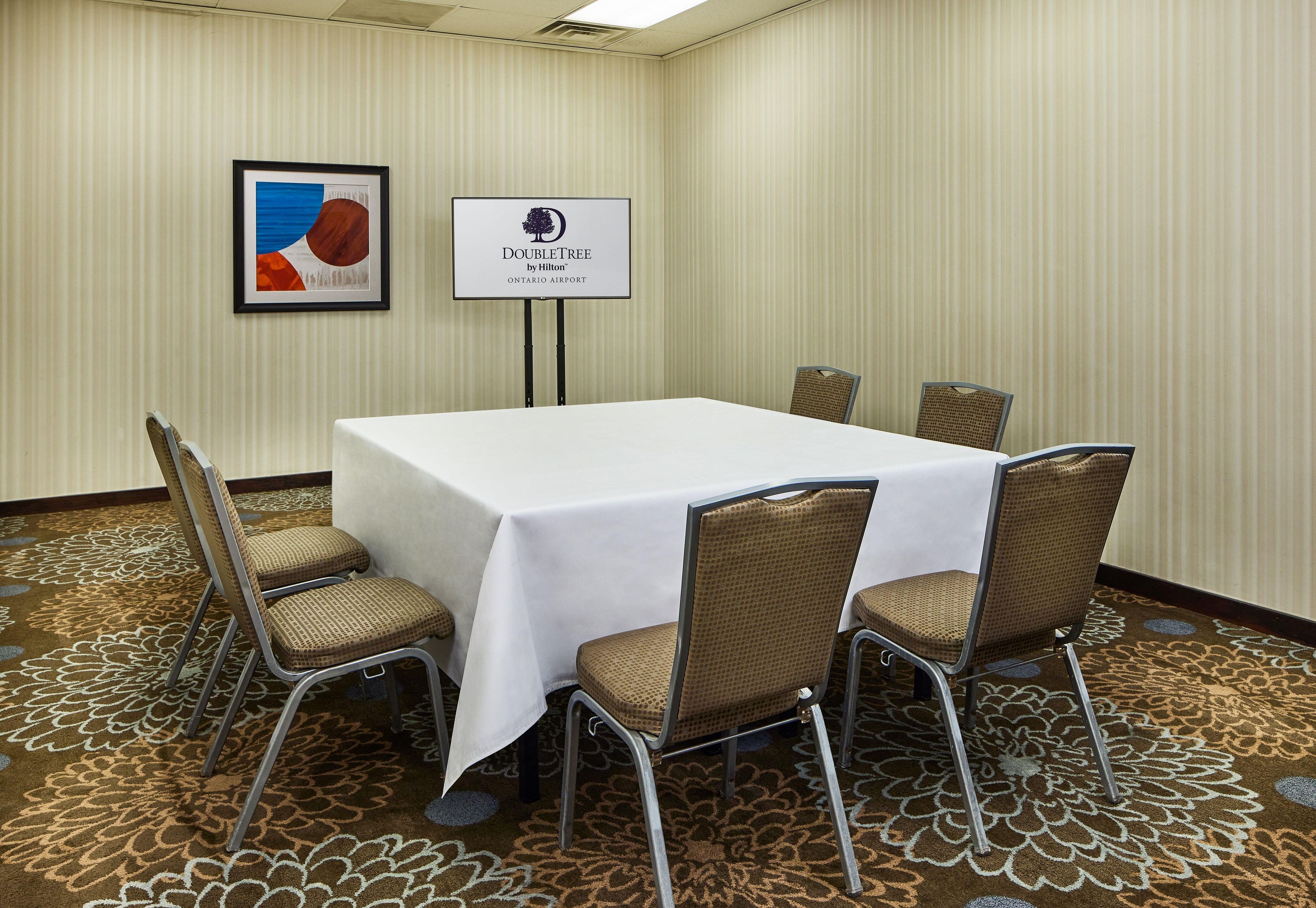 A conference room with a white table, six chairs, a framed artwork, and a sign indicating the location at Ontario Airport.
