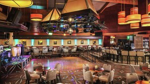 Um lobby amplo com vários espaços de estar, um palco com equipamentos de iluminação e uma área de bar com televisão.