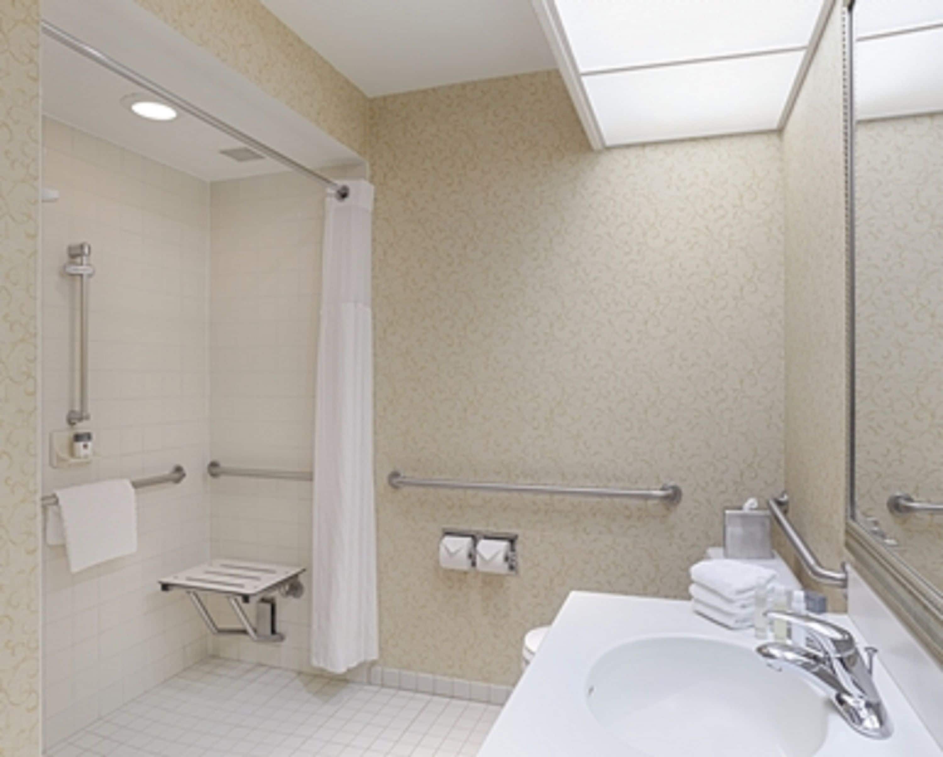 Baño con ducha, barras de apoyo, lavabo e inodoro.
