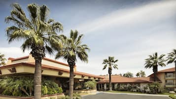 A hotel with a courtyard, palm trees, and a building with a red-tiled roof.