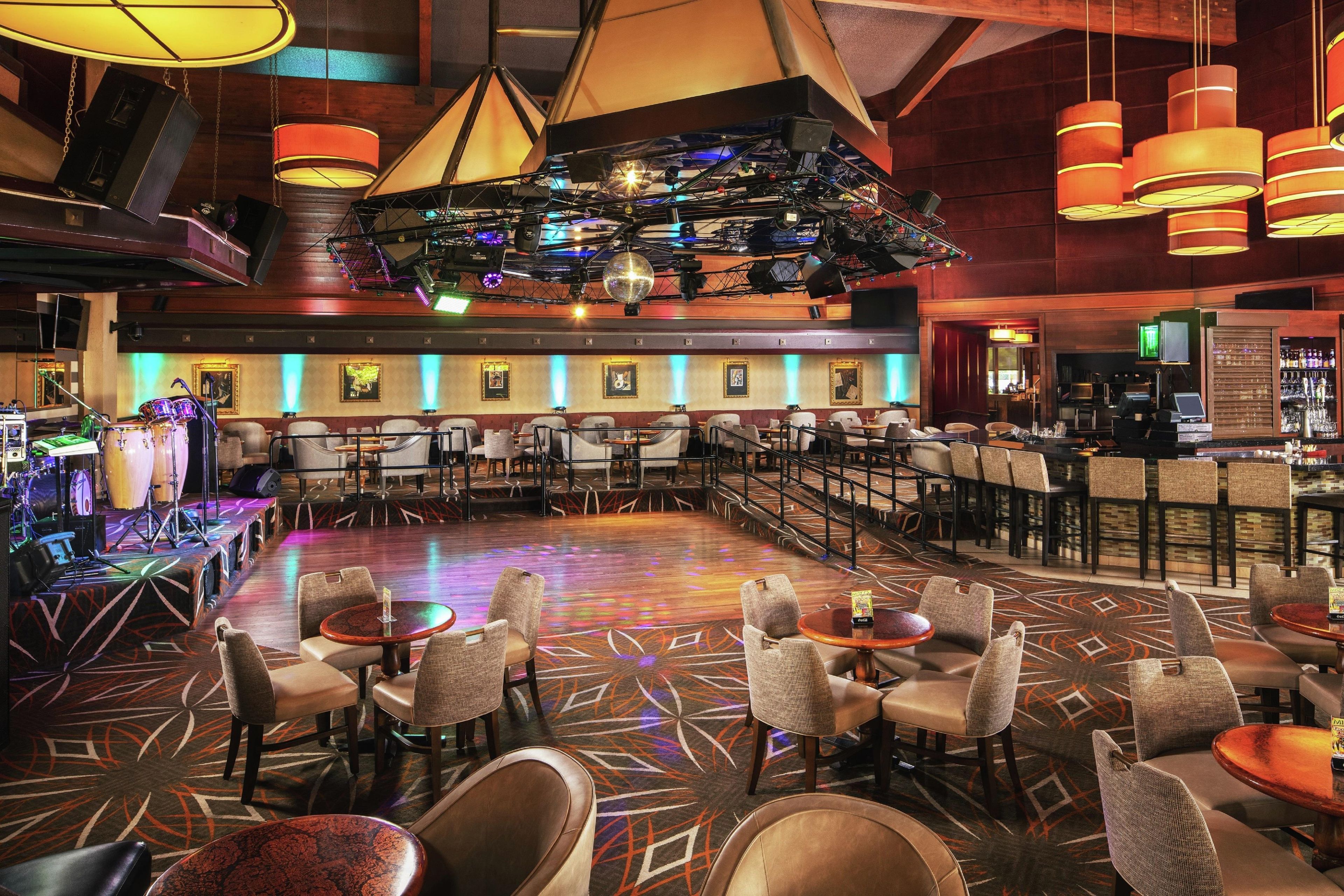 A spacious bar area with multiple seating arrangements, including tables and chairs, and a stage with musical equipment.