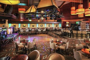 A spacious bar area with multiple seating arrangements, including tables and chairs, and a stage with musical equipment.