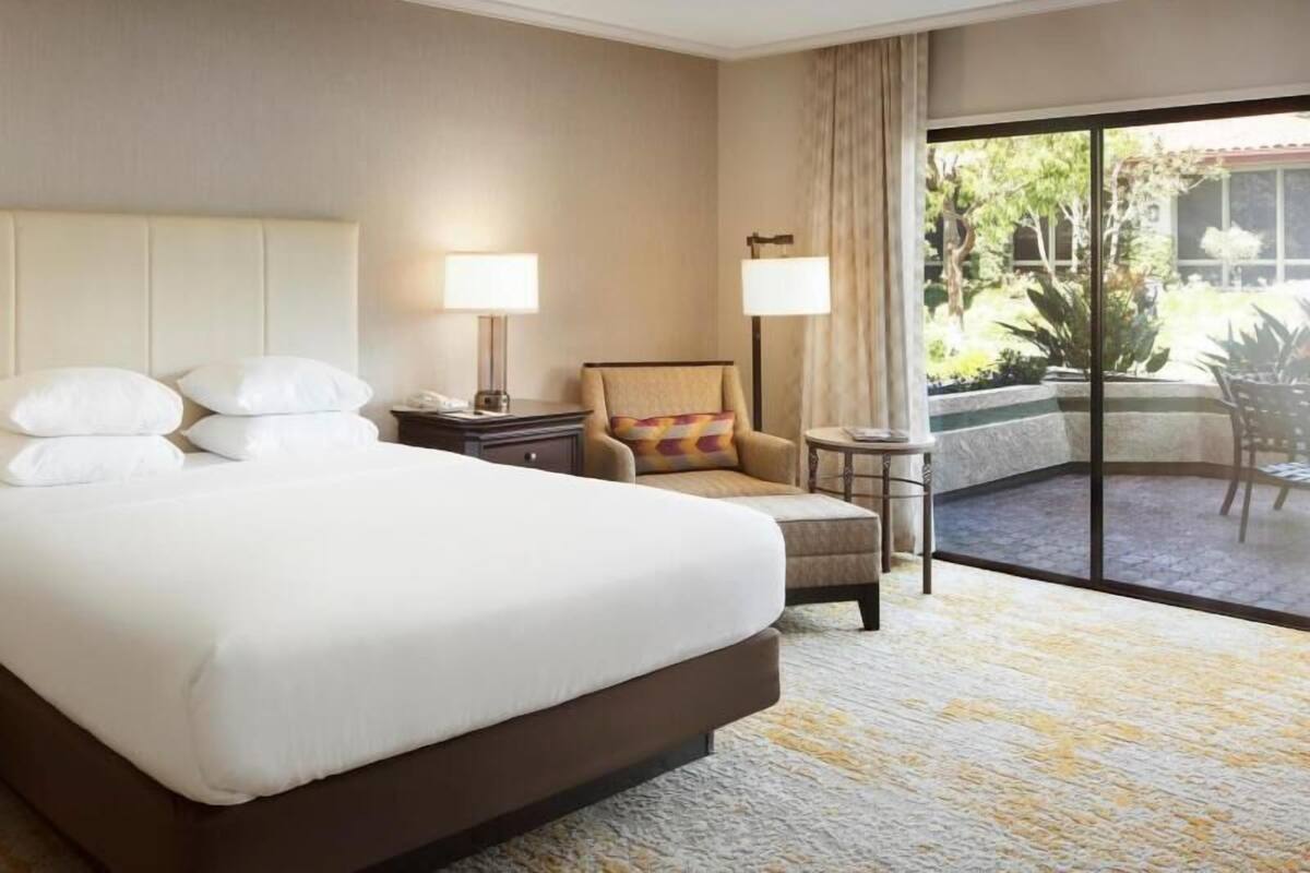 Habitación de hotel con una cama grande, una silla, una mesita y vistas al exterior.