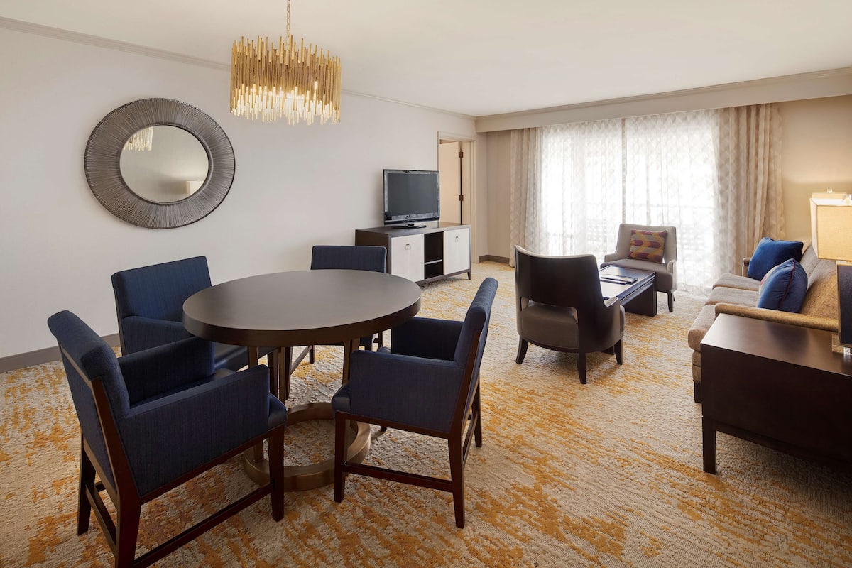 Ein Hotelzimmer mit einem runden Esstisch, vier Stühlen, einer Couch, einem Fernseher und einem großen Spiegel an der Wand.