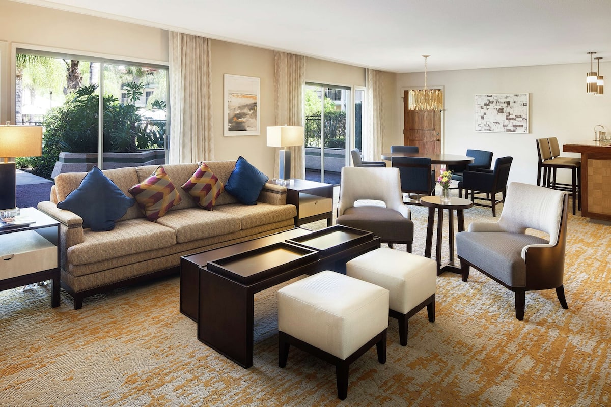 Ein modernes Hotelzimmer mit einer Couch, Hocker, einem Couchtisch und einem Essbereich mit Stühlen und einem Tisch.