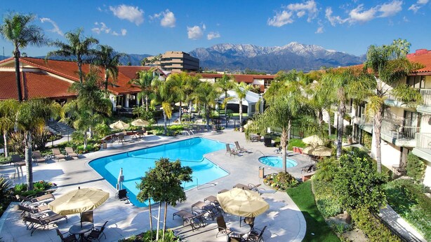 Um resort com piscina grande, palmeiras e vista para as montanhas.