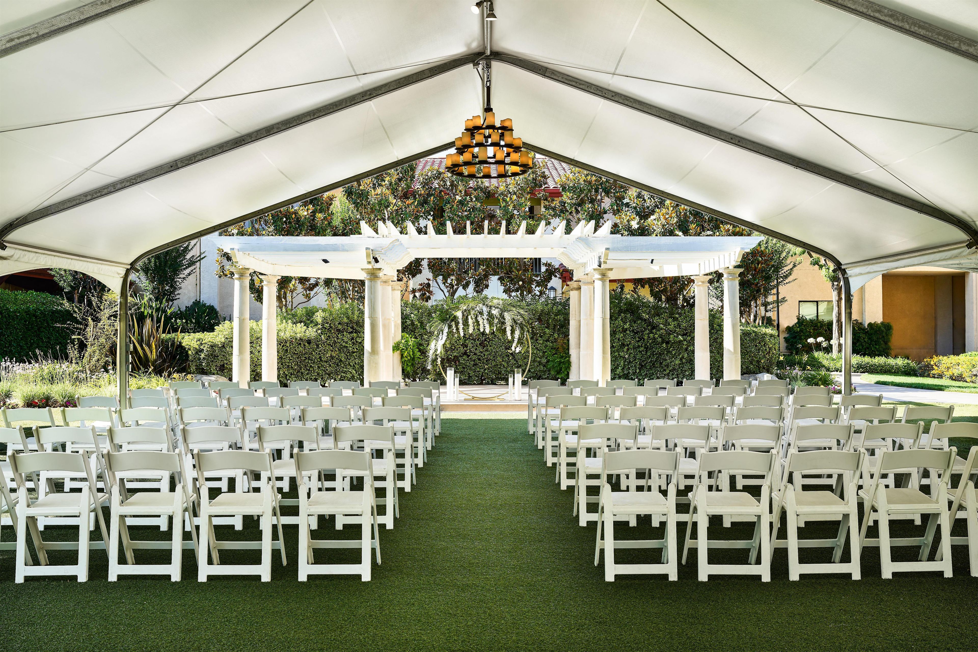 A tented outdoor venue with rows of white chairs and a central aisle leading to a decorative archway.