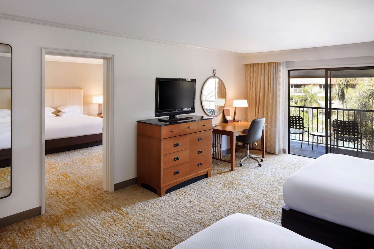 Ein Hotelzimmer mit Bett, Schreibtisch mit Computer, Fernseher, Kommode und Balkon mit Gartenmöbeln.