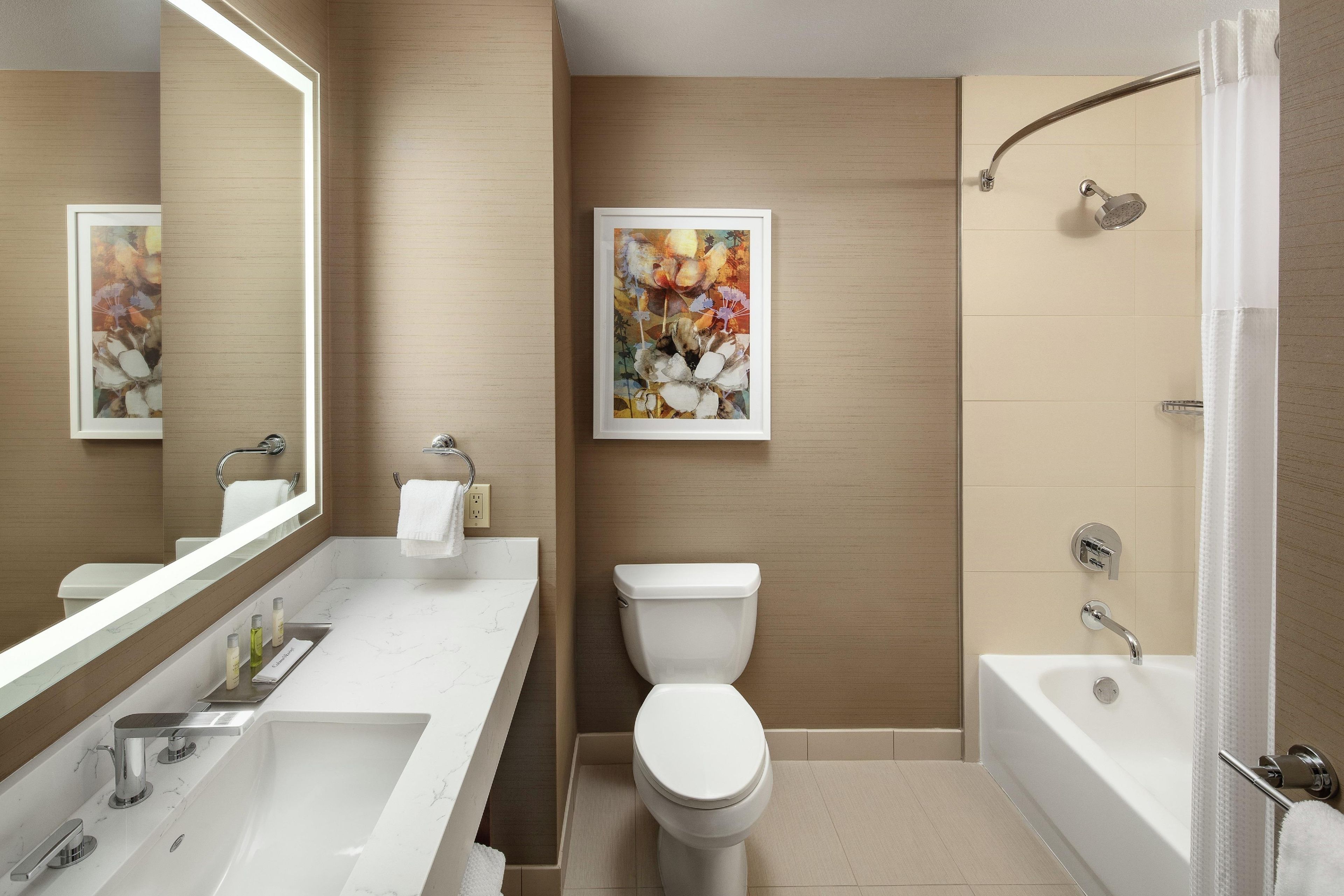 Ein modernes Badezimmer mit einem großen Spiegel, einem weißen Waschbecken, einer Toilette und einer Badewanne.