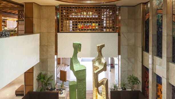 Een moderne lobby met een houten plafond, een centrale sculptuur en zithoeken.