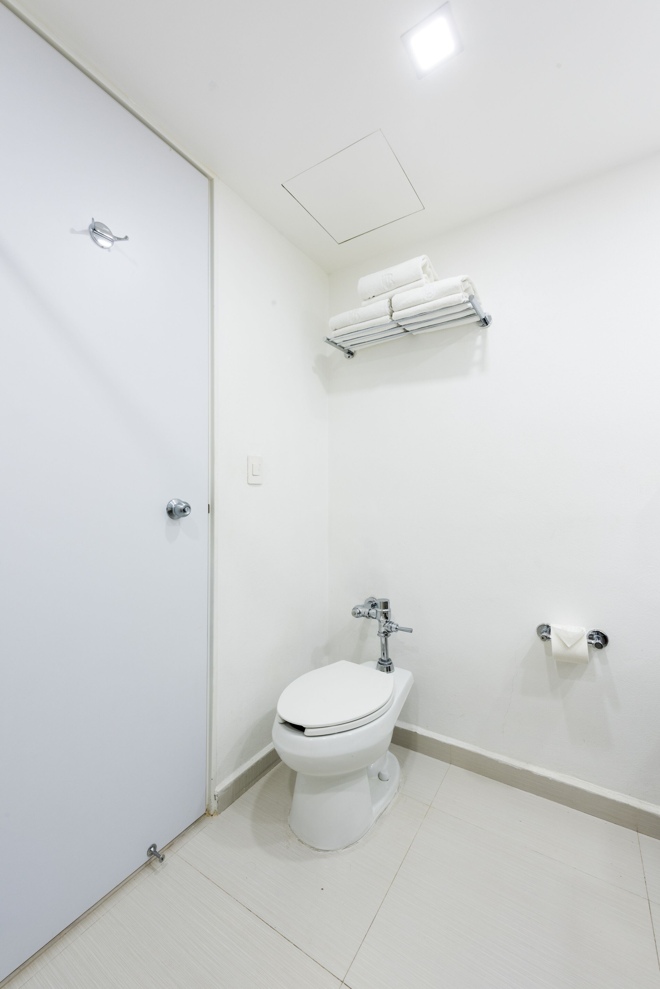 Un baño pequeño y limpio con inodoro, toallero y dispensador de papel higiénico.