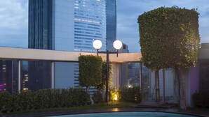 Een modern gebouw met een glazen gevel die reflecteert, een zwembad en verzorgde groenvoorziening.